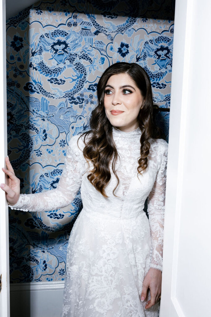 Bride in a lace wedding gown leaning gracefully on a vintage doorframe at The Bryan Museum bridal suite in Galveston, Texas