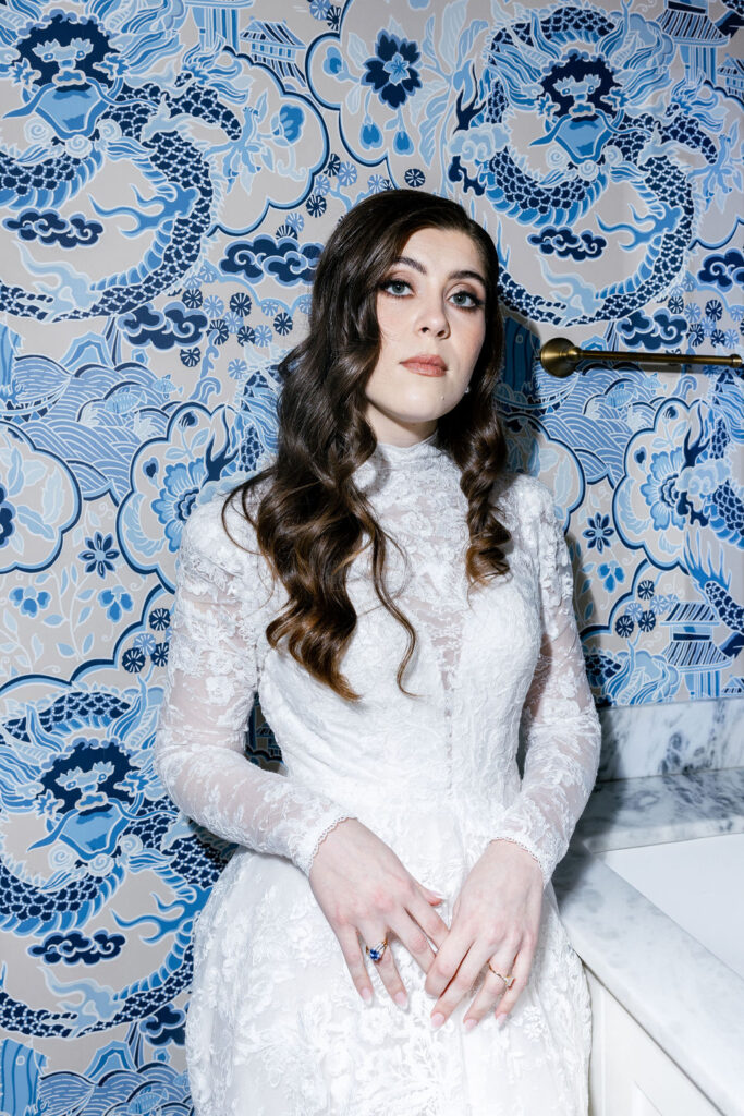 Bride in a lace wedding dress posing against a vibrant blue dragon-patterned wallpaper in the bridal suite at The Bryan Museum in Galveston, Texas