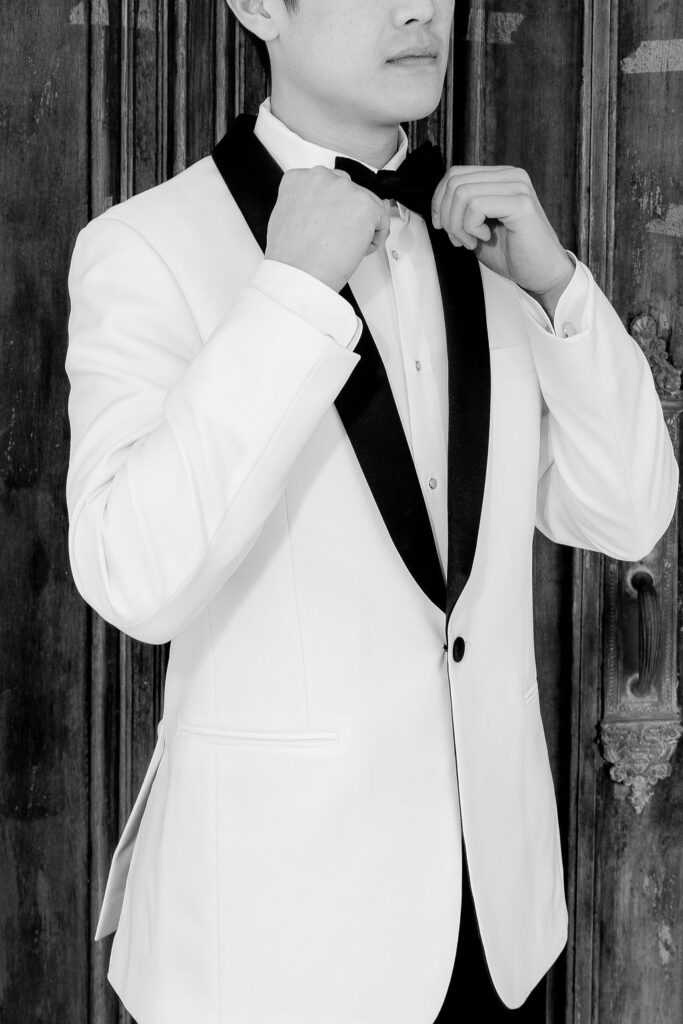Black and white close-up of groom fixing his collar before his Bryan Museum wedding, captured outside Sacred Heart Catholic Church in Galveston.
