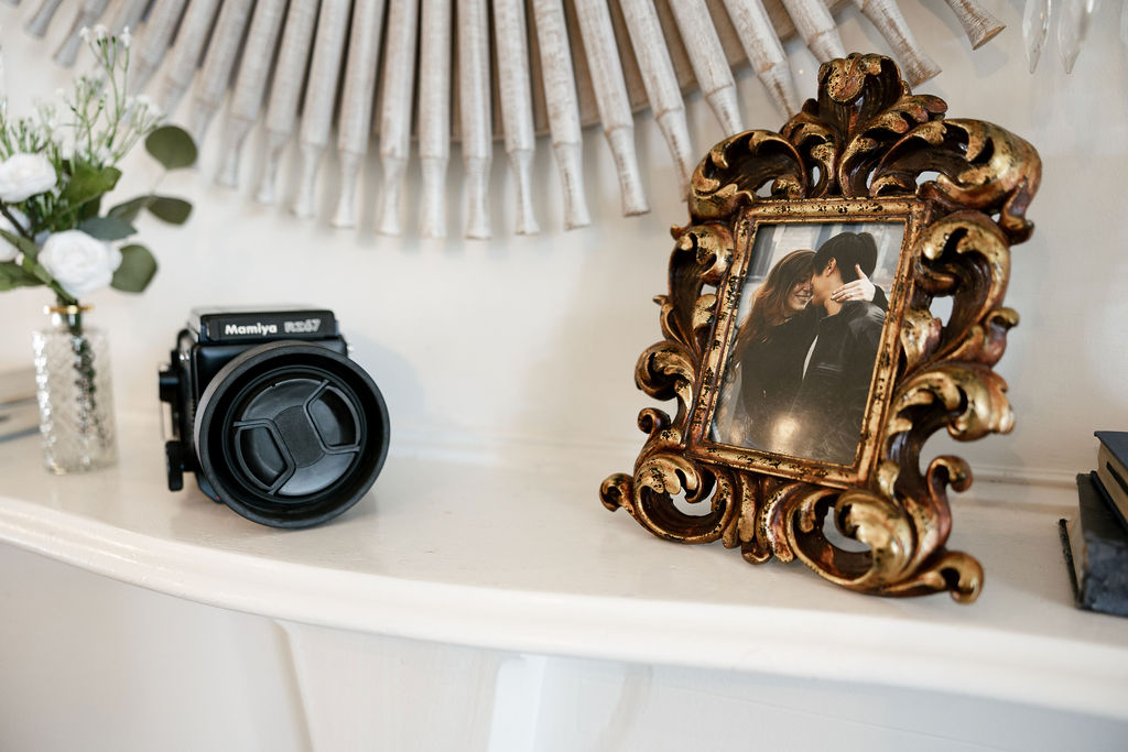 Vintage photo frame with a couple's portrait, Mamiya camera, and floral decor on a mantel in the bridal preparation room at The Bryan Museum in Galveston, Texas.