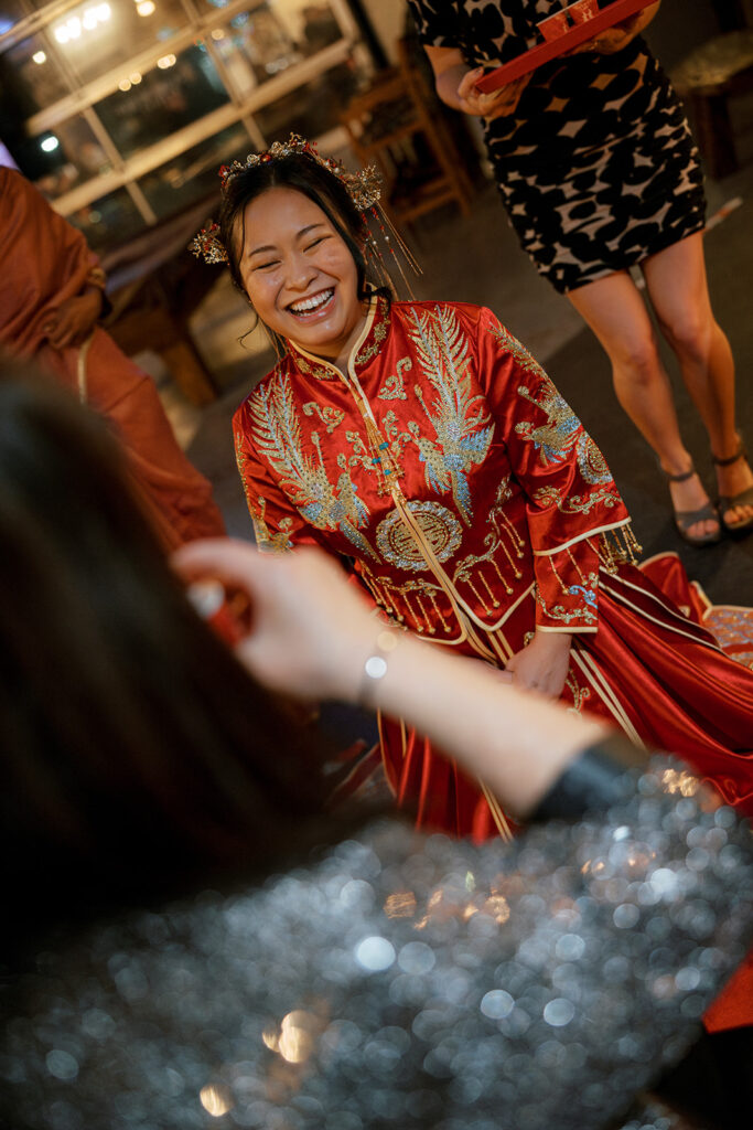 Jessie smiles while she kneels in traditional red and gold outfits during the tea ceremony before their Bryan Museum garden wedding.