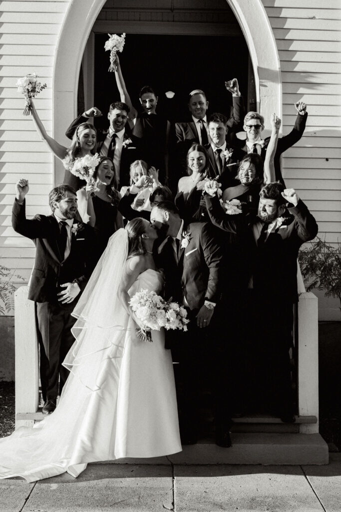 Wedding couple with the wedding party take a black and white photo during the Real Wedding at Galveston City National Bank Museum