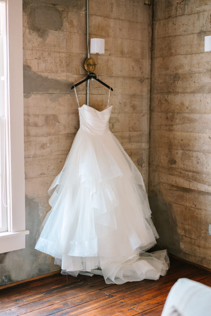 Elegant white wedding dress hanging against rustic stone walls at The Artisan.