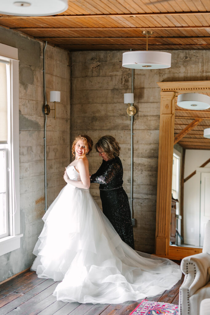 Bride smiling in her gown while her mother adjust the dress during a wedding at The Artisan.