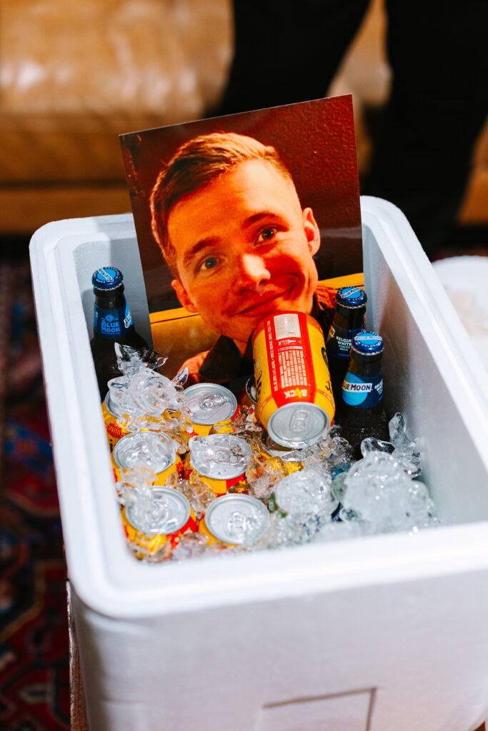 Cooler filled with drinks and a humorous cutout face at a wedding at The Artisan