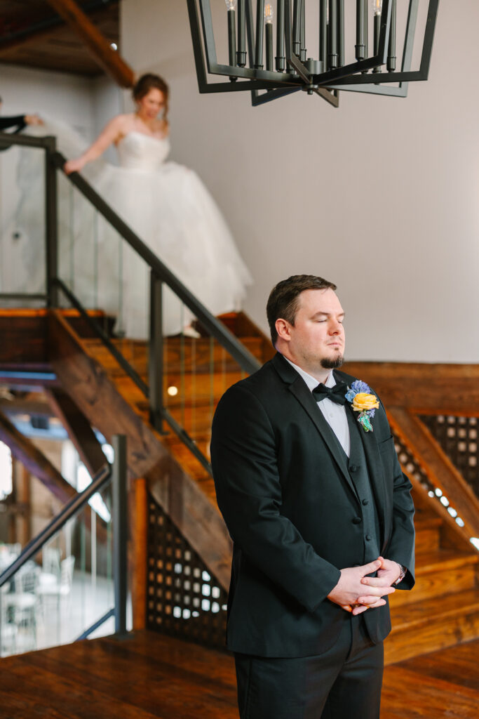 Groom waiting at the bottom of the staircase for the first look at The Artisan.