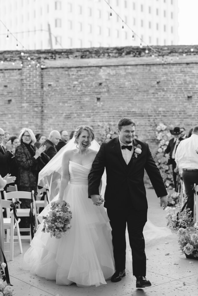 Black and white photo of bride and groom walking hand in hand after their wedding at The Artisan.