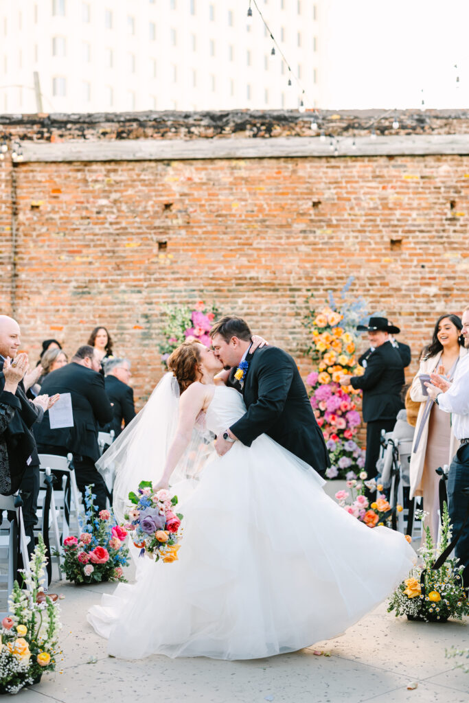 Groom dips the bride for a kiss in front of guests during a wedding at The Artisan.