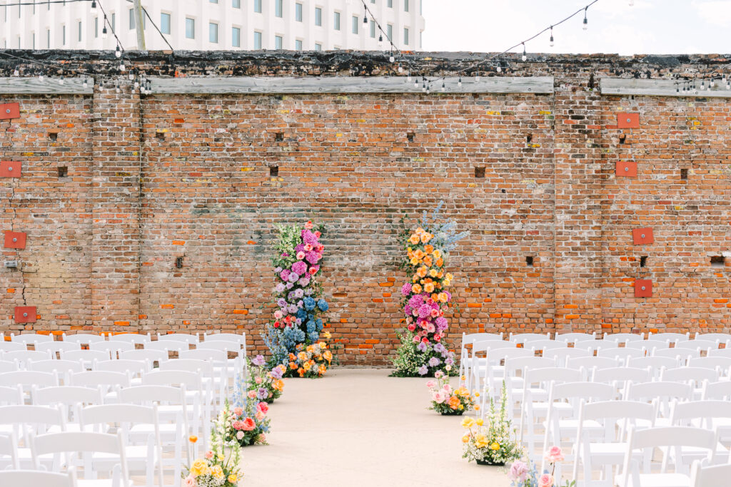 Ceremony setup with colorful floral arch and white chairs at a wedding at The Artisan.