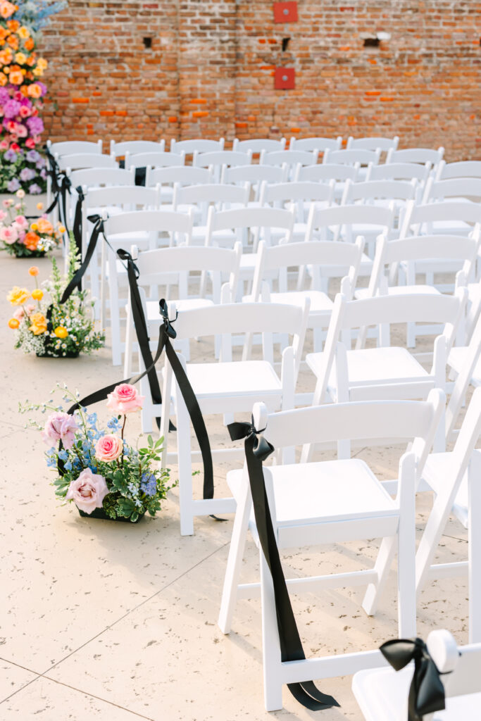 White chairs with black ribbons and floral accents lining the aisle at The Artisan wedding.