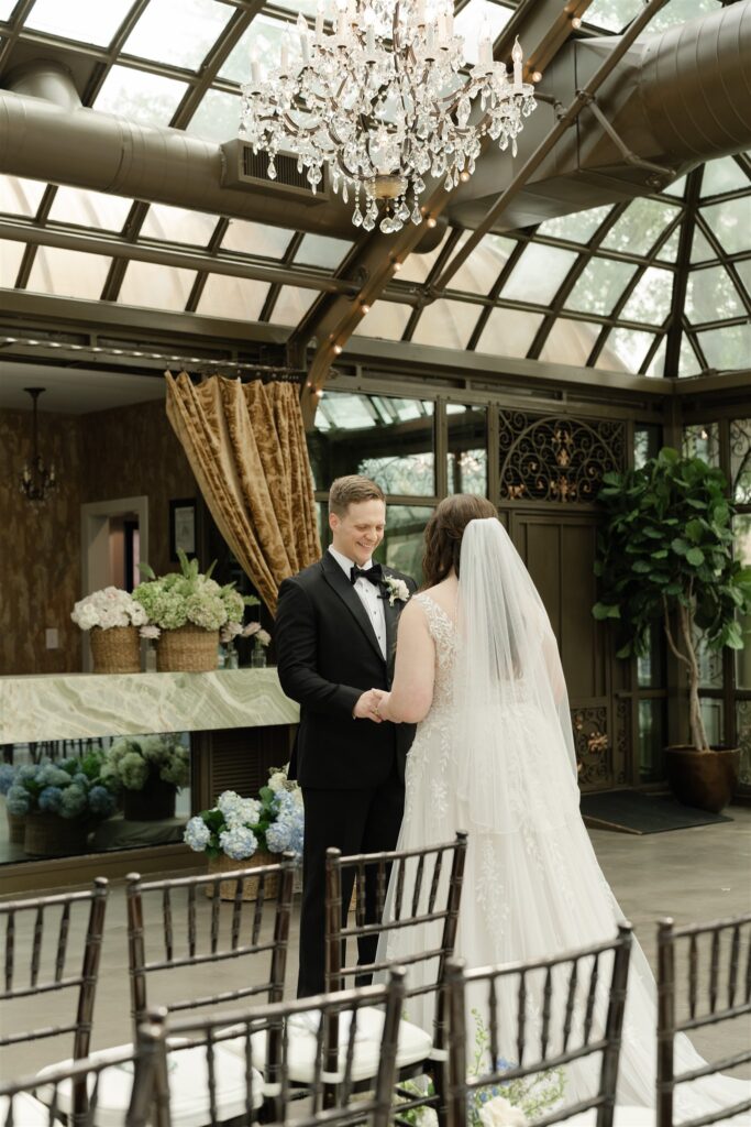 Groom smiles during their first look in the elegant glass conservatory at The Bryan Museum.