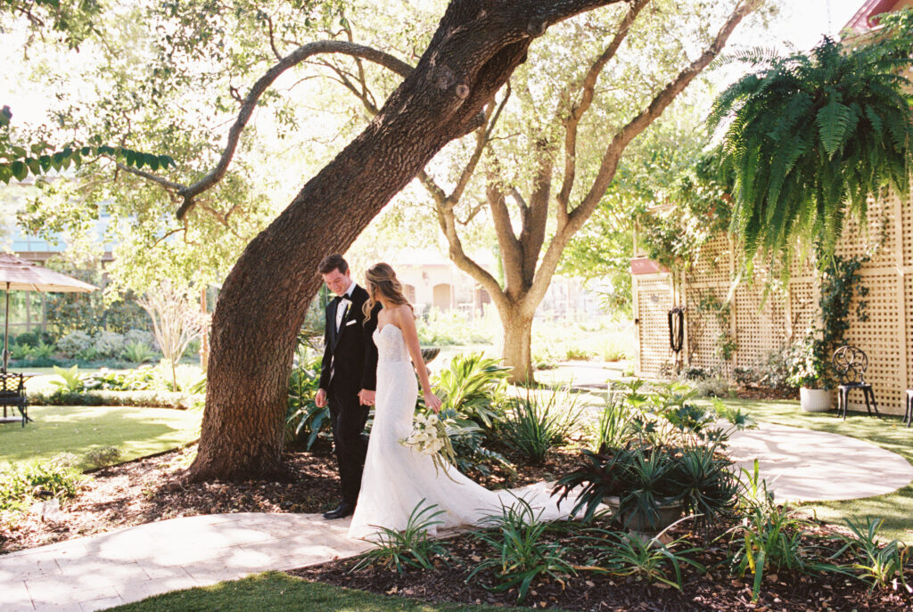Bride and groom walks together beneath the trees during romantic fall wedding portraits at The Bryan Museum.