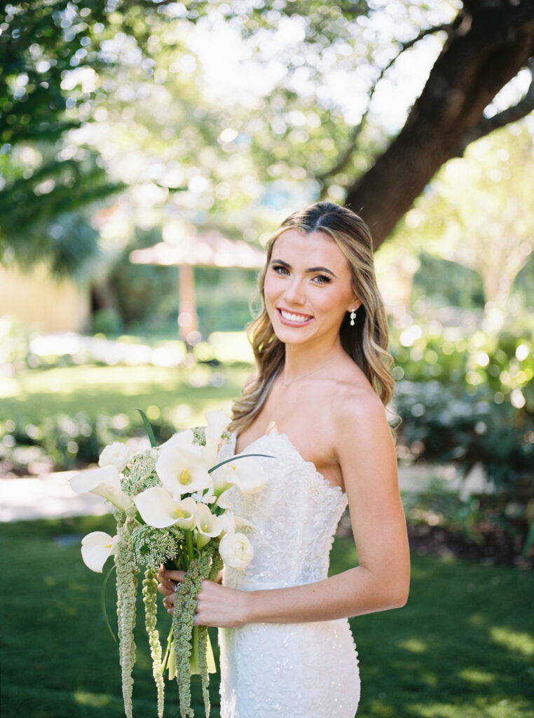 Bride smiling outdoors beneath trees during romantic fall wedding portraits at The Bryan Museum.