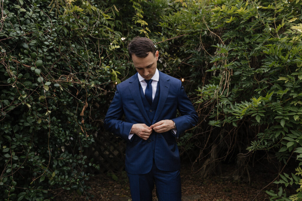 Groom in navy suit preparing for his Carr Mansion wedding in the garden.